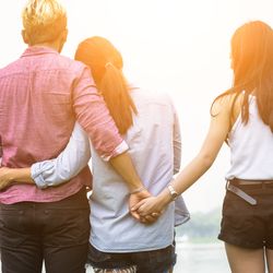 A couple with their arms around each other, but the man is holding hands with another woman behind his partner's back