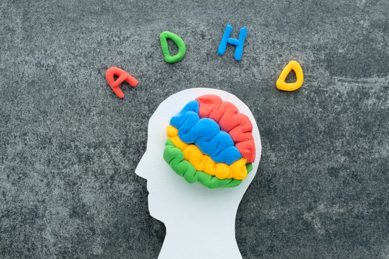 paper cutout of a human head with blue, red, green and yellow plasticine in the shape of a brain; the letters A D H and D are spelled out in plasticine above on a grey stone surface