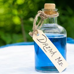 blue liquid in glass bottle labeled "drink me" with blue alarm clock in the background