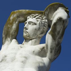 statue of a discus thrower, visible from the torso up against a clear blue sky