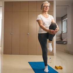 Elderly woman stands on one leg in a tree pose