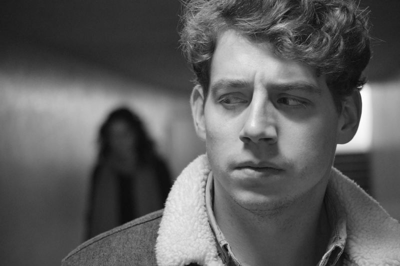 Black and white photo of man looking over his shoulder, worried, at a woman blurred in the background