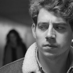 Black and white photo of man looking over his shoulder, worried, at a woman blurred in the background