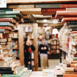 books in a library on brown wooden shelf with people talking.