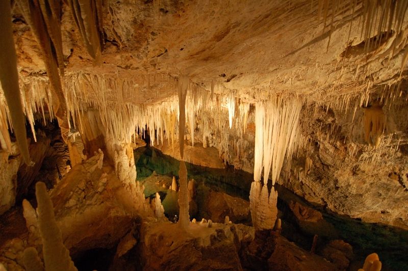 Large underground cavern filled with stalactites and stalagmites with bright blue water at the bottom.