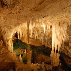 Large underground cavern filled with stalactites and stalagmites with bright blue water at the bottom.