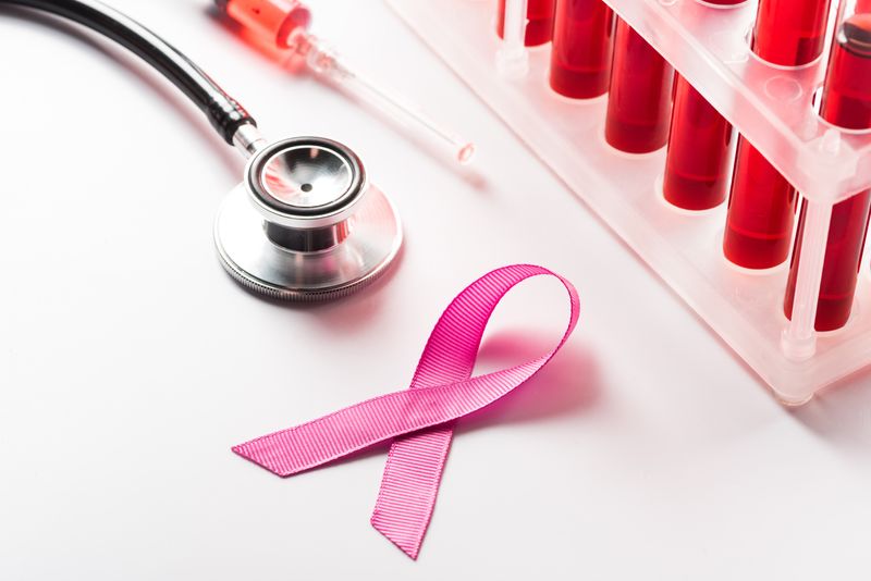 pink breast cancer awareness ribbon next to stethoscope and rack of tubes containing red liquid