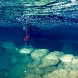 underwater bridge, photographed from just below the surface; someone's legs are visible as they stand on the stones of the bridge