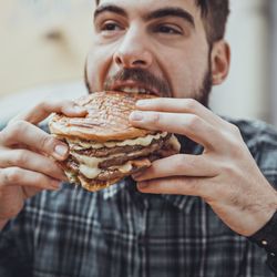 man wearing plaid shirt eating a burger