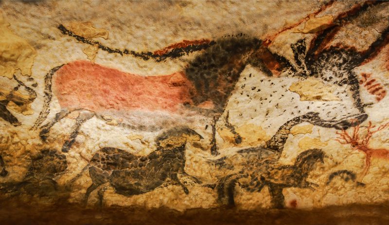 A photo showing the cave art at the Lascaux Cave in France. The image shows a horse painted in red medium being imposed on the black outline of a large bull-like animal. Below it are smaller black representations of other horse-like animals. 