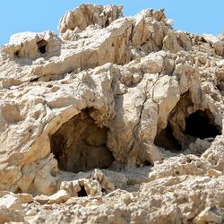 A photo of a series of caves in a rocky face of a cliff. The image shows two of the caves surrounding by craggy pale rocks. The scene is completely absent of any vegetation.  