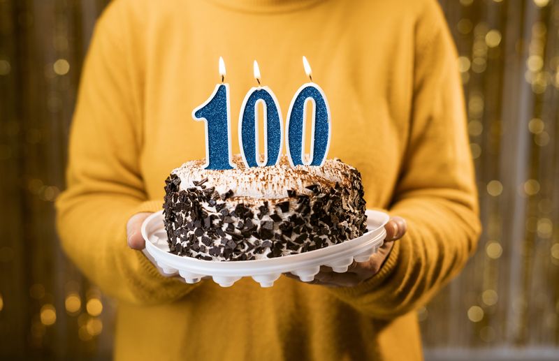 Person holding a cake with "100" candles