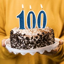 Person holding a cake with "100" candles