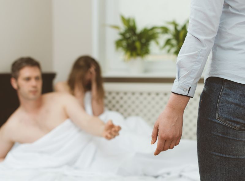 woman catches male partner in bed with another woman; close shot of the woman's arm and leg as she apparently walks in on a man and woman in bed; the couple in bed are out of focus in the background