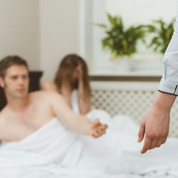 woman catches male partner in bed with another woman; close shot of the woman's arm and leg as she apparently walks in on a man and woman in bed; the couple in bed are out of focus in the background