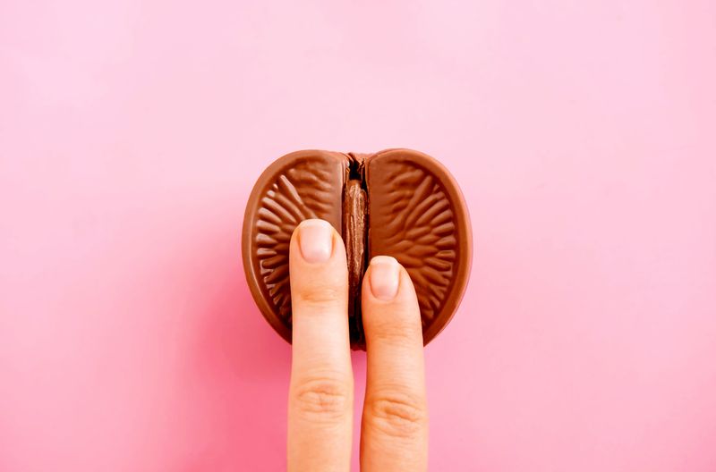 two fingers on a chocolate orange that has been cut in half, on a pink background