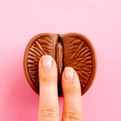 two fingers on a chocolate orange that has been cut in half, on a pink background