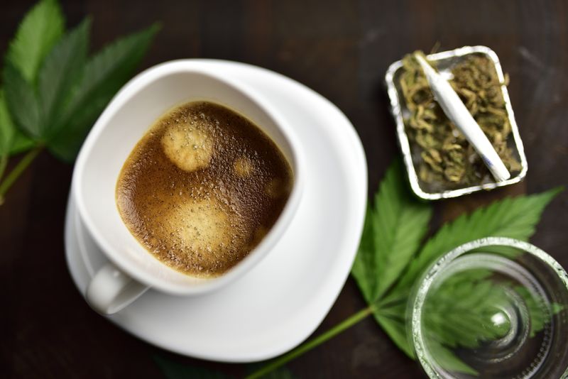 white coffee cup on wooden butcher cutting board with joint, cannabis bud and cannabis leaf