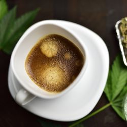 white coffee cup on wooden butcher cutting board with joint, cannabis bud and cannabis leaf