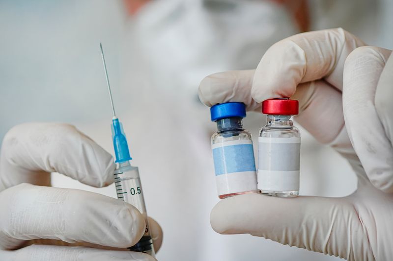 concept image for a combined vaccine, close up of doctor holding two vaccine vials and a syringe in white-gloved hands