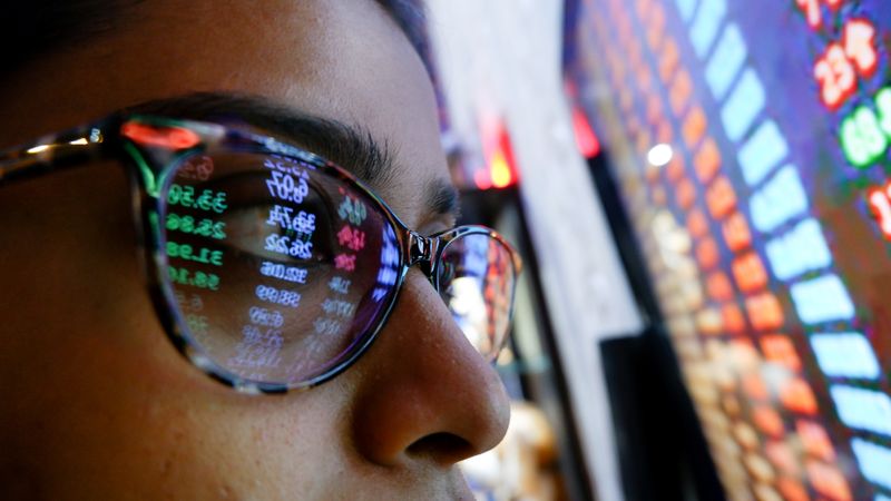 A cryptocurrency investor wearing sunglasses looks closely at a screen of graphs and money