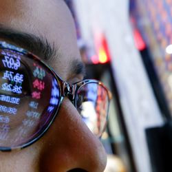 A cryptocurrency investor wearing sunglasses looks closely at a screen of graphs and money