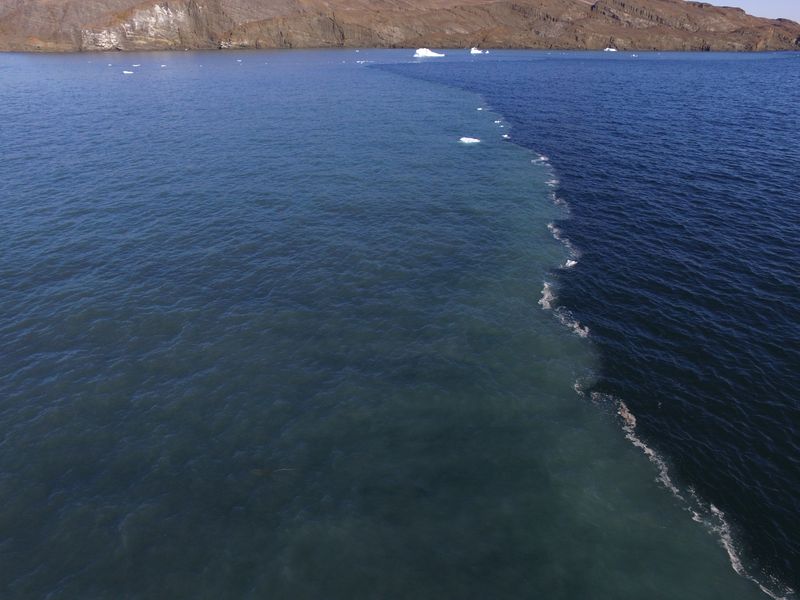 Drone aerial image of the sharp front dividing clear ocean waters from a turbid freshwater river plume fed by the melting of the Greenland Ice Sheet