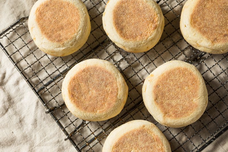 Aerial shot of six English muffins arranged on a cooling rack on a cream tablecloth