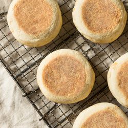 Aerial shot of six English muffins arranged on a cooling rack on a cream tablecloth