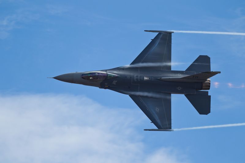 An F-16 fighter jet doing a flying maneuver in the sky. 