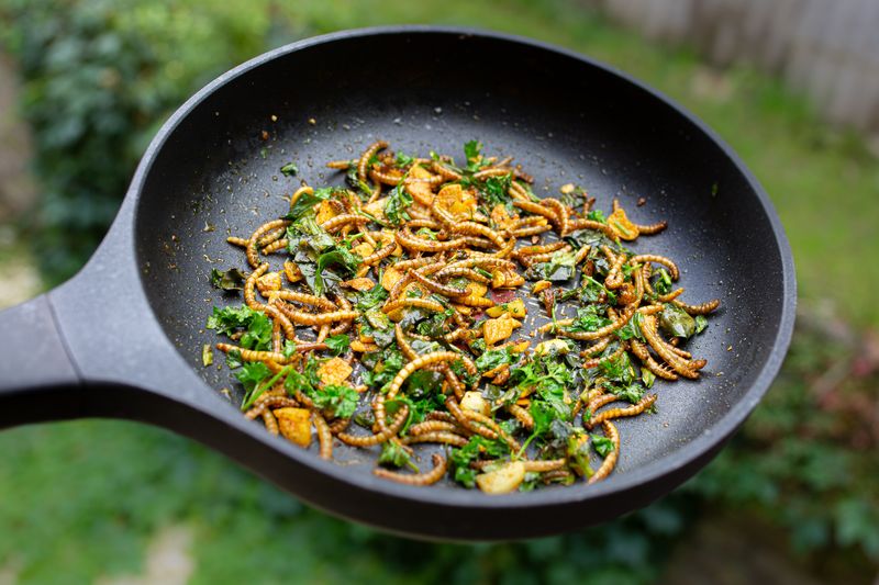 edible mealworms frying in a pan with some green herbs