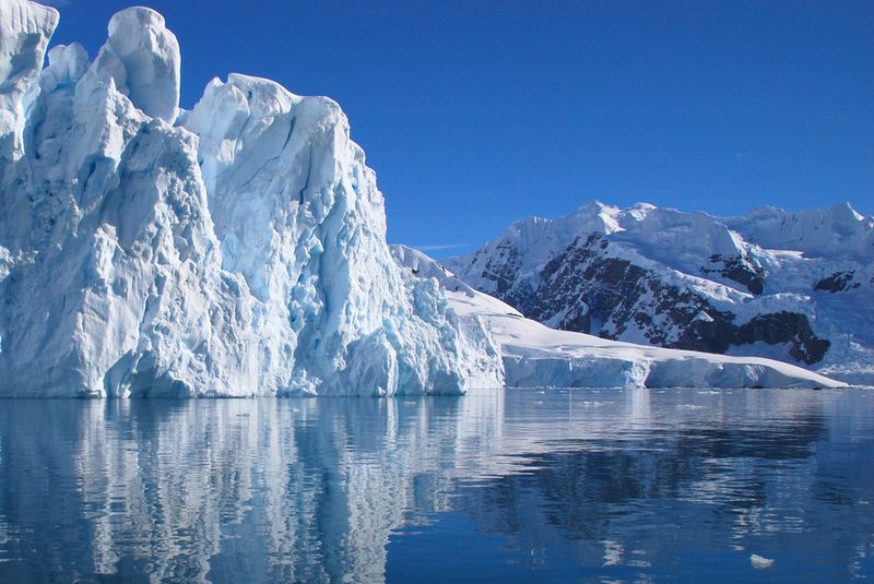 Large glacier, with blue sky in the background and water in the foreground.