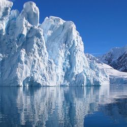 Large glacier, with blue sky in the background and water in the foreground.