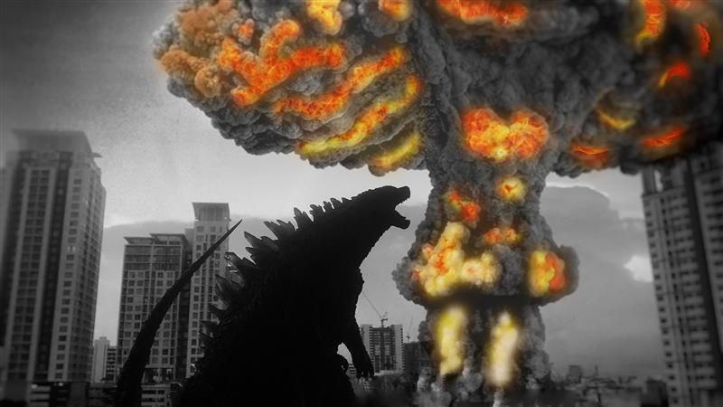 The image shows the silhouette of Godzilla standing in the middle of a city with towering skyscrapers either side. The monster has its head raise and mouth open and in the background a large mushroom cloud is visible. The mushroom cloud contains the only for of color in the image, as its structure is highlighted with flames. 