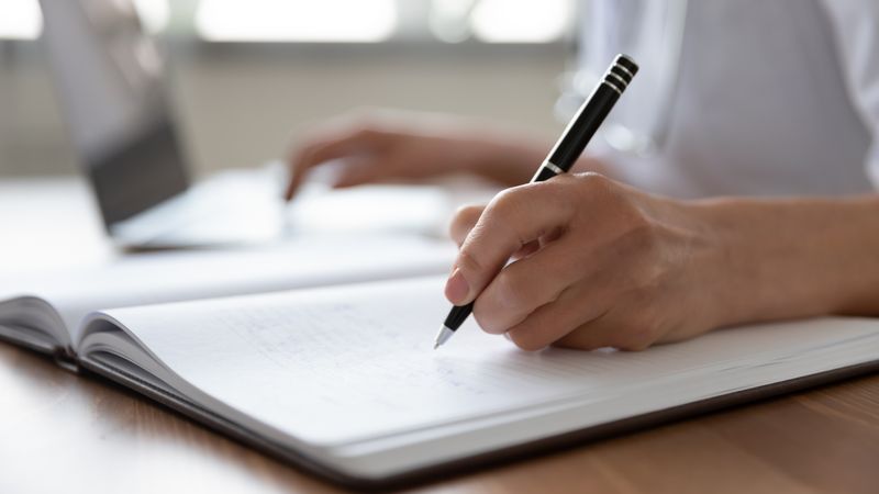 A person holding a pen and writing by hand into a notebook