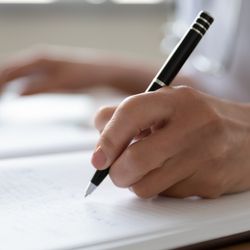 A person holding a pen and writing by hand into a notebook