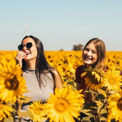 three women smiling and laughing together in a field of sunflowers on a sunny day