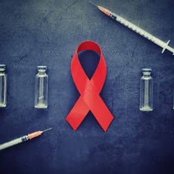 concept of injection for HIV. Red HIV awareness ribbon with three injection vials on either side of it on a dark grey surface, with two syringes