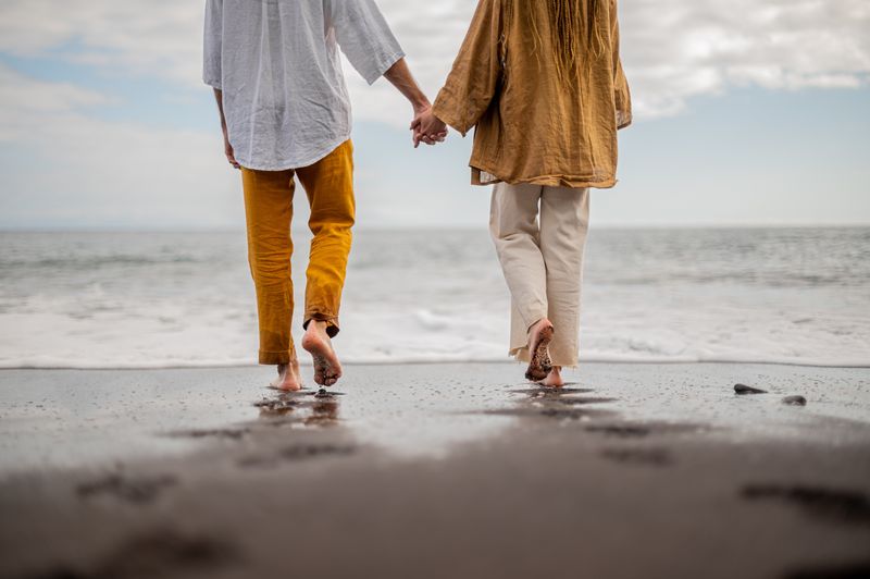 couple with their backs to the camera holding hands on a beach