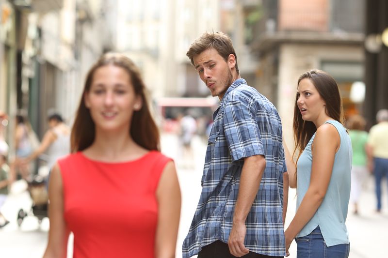 Disloyal man walking with his girlfriend and looking amazed at another girl