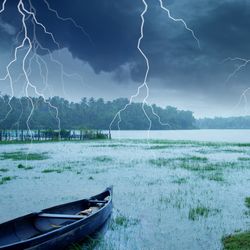 Flashes of lightning in a storm hitting a deserted lake with a wooden boat in