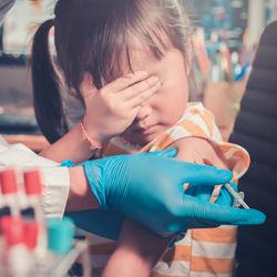 little girl covers her eyes while doctor injects her with a vaccine