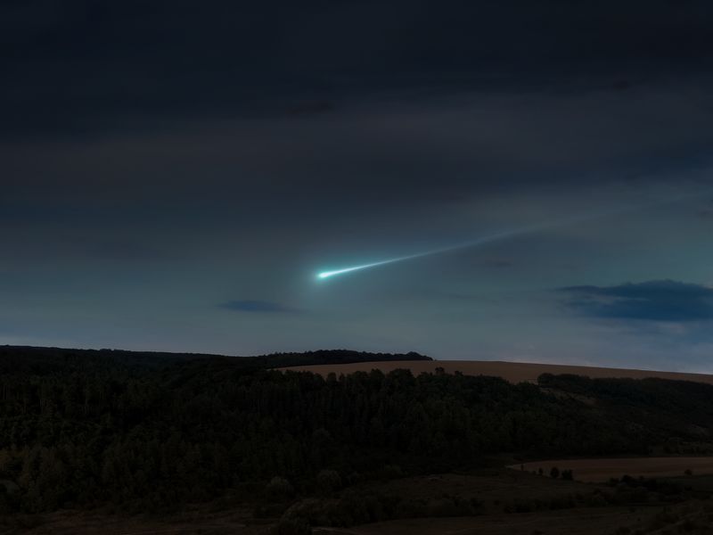 Blue meteor trail in the evening sky over the hills