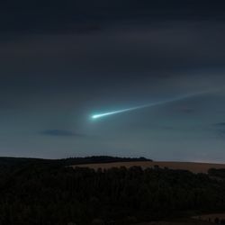 Blue meteor trail in the evening sky over the hills