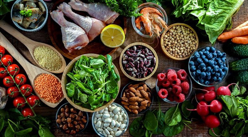 Fruit, vegetables, meat, fish, nuts, beans, and grains arranged on a wooden floor