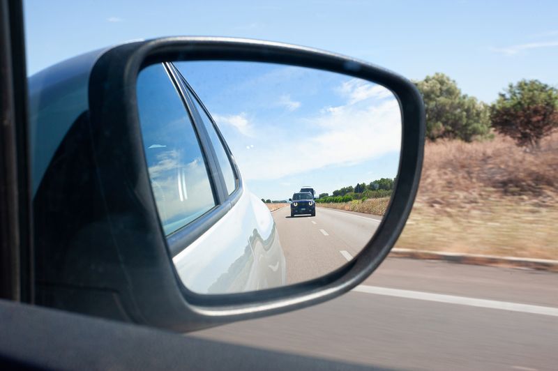 close-up of a car's side-view mirror, with a black car in the distance