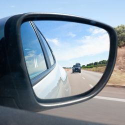 close-up of a car's side-view mirror, with a black car in the distance