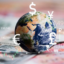 globe on a table covered with bank notes, with numbers, currency symbols and graphs to indicate the stock market overlaid on top in white, green and red