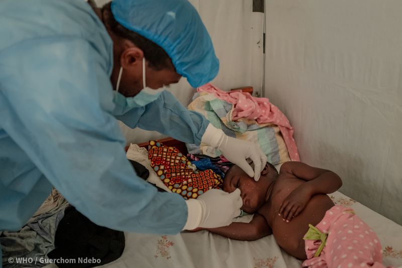 Tresor, a health worker wearing blue scrubs, a mask, and surgical cap, checks on two-year-old Ibrahim, who is being treated for mpox, at the Nyiragongo General Referral Hospital, north of Goma in the Democratic Republic of the Congo (DRC) on 14 August 2024.