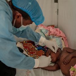 Tresor, a health worker wearing blue scrubs, a mask, and surgical cap, checks on two-year-old Ibrahim, who is being treated for mpox, at the Nyiragongo General Referral Hospital, north of Goma in the Democratic Republic of the Congo (DRC) on 14 August 2024.